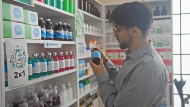 A young man with a beard examines a product at a pharmacy's medicine shelf. clipart