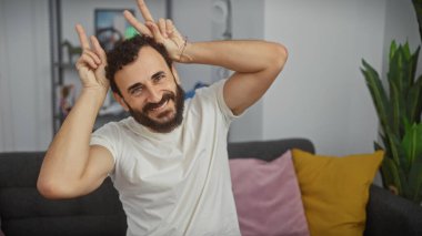 Neşeli bir adam tavşan kulağı hareketi yapıyor, sıcak bir oturma odasında oturuyor..