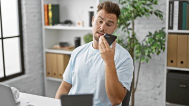 Mavi gömlekli İspanyol adam modern ofis ortamında sesli mesaj gönderiyor.