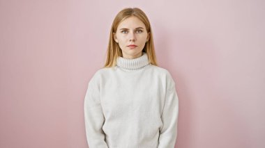 Sarı saçlı, mavi gözlü, pembe arka planda izole edilmiş beyaz bir süveter giyen sakin, beyaz bir beyaz kadın.