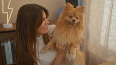 Genç bir kadın, sevimli Pomeranian 'ı ile sıcak bir oturma odasında vakit geçirmekten zevk alıyor..