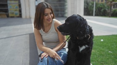 Güneşli bir günde, şehir parkında labrador köpeğiyle eğlenen güzel, genç bir İspanyol kadın..