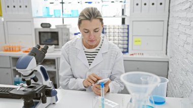 Kafkasyalı bir kadın bilim adamı, kapalı alandaki parlak bir laboratuvar ortamında örnekleri analiz ediyor..