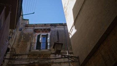 Bari, İtalya 'da tarihi bir sokak, açık panjurları ve mavi gökyüzü arkaplanı olan yıpranmış bir binanın cephesini gösteriyor..