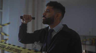 Düşünceli bir ifade ve bir el feneri taşıyan loş ışıklı bir suç mahallini inceleyen İspanyol dedektif.