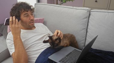 Genç bir İspanyol adam, oturma odasındaki bir kanepede dinlenirken kucağında bir kedi ve yakınındaki bir dizüstü bilgisayarla bir sesli mesaj dinler..