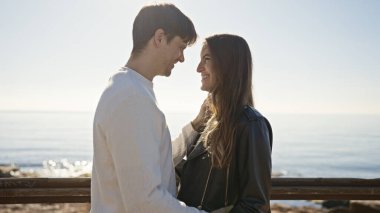 Deniz kenarında kucaklaşan sevgi dolu bir çift kumsalda bir kadın ve bir erkek arasındaki huzurlu anın altını çiziyor..