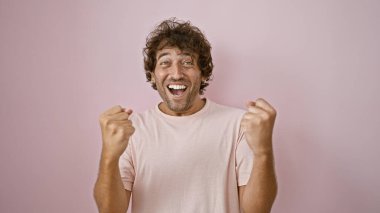 Neşeli, genç, İspanyol bir adam, pembe bir arka plana yumruk sallayarak kutluyor..