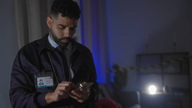 Ciddi bir erkek dedektif akıllı telefon kullanırken loş bir suç mahallinde kanıt inceler..