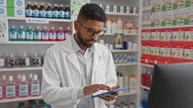 Beyaz önlüklü Afrikalı Amerikalı eczacı modern bir eczanenin içinde dijital tablet kullanıyor.