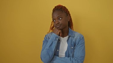 A thoughtful young african american woman stands isolated against a vibrant yellow background, exuding calm and beauty. clipart