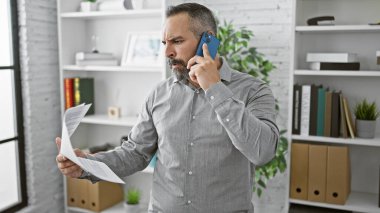 Elinde belge tutarken telefonda konuşan, sakallı, kır saçlı, olgun İspanyol bir adam..