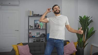 Neşeli sakallı bir adam modern bir salonda tek başına dans ediyor, kendine güven ve neşe saçıyor..