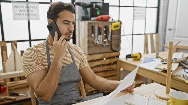 Telefondaki sakallı İspanyol adam bir marangozhane atölyesinin planlarını tutuyor.
