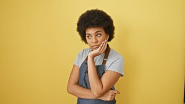 Sarı arka planda kıvırcık saçlı, sıradan güzelliği canlandıran düşünceli Afrikalı Amerikalı kadın..