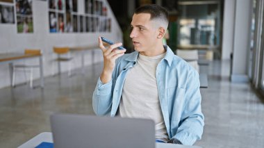 Yakışıklı genç İspanyol bir adam akıllı telefon kullanarak kapalı bir üniversitede sesli mesaj yolluyor..