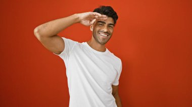 Sakallı yakışıklı, genç, İspanyol bir adam canlı kırmızı bir duvara karşı şakacı bir şekilde selam veriyor..