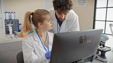Laboratuvar önlüklü bir kadın ve erkek, parlak bir laboratuvar ortamında bilgisayardaki verileri analiz ediyor.