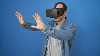 Mavi arka planda sanal gerçeklik kulaklığı kullanan İspanyol sakallı adam, günlük kot giysisi giyen vr teknolojisini keşfediyor..