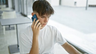 Kafkasyalı genç bir erkek, parlak modern bir sınıfın içindeki masada otururken akıllı bir telefonla konuşuyor..