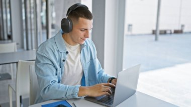 Üniversite kütüphanesinde dizüstü bilgisayar ve kulaklıkla çalışan yakışıklı bir İspanyol..