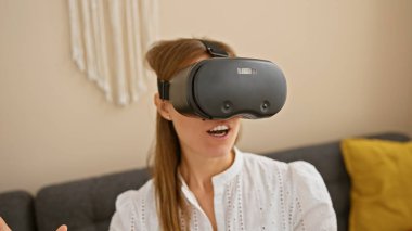 Modern bir oturma odasında sanal gerçeklik deneyimi yaşayan beyaz bir kadın..