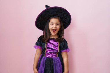 Cadı kostümü giymiş tapılası İspanyol kız, ağzı açık, şaşırmış ve korkmuştu. İzole edilmiş pembe arkaplan üzerinde sürpriz ifade.