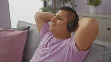 Rahat İspanyol adam, rahat bir oturma odasında kulaklıkla müzik dinliyor..
