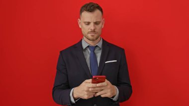 Takım elbiseli bir işadamı, canlı kırmızı bir arka plana karşı akıllı telefon kullanıyor..