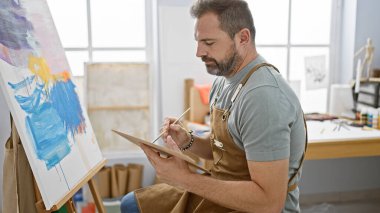 Parlak bir sanat stüdyosunun içinde gri saçlı yakışıklı, İspanyol bir adam..