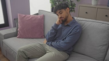 Modern bir oturma odasındaki kanepede sakallı düşünceli genç bir adam..