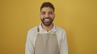 Sarı duvara gülümseyen önlük takan sakallı yakışıklı İspanyol adam.