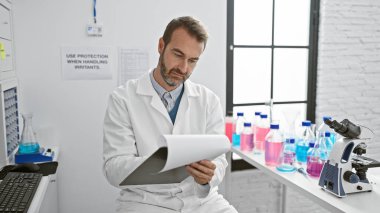 İspanyol bilim adamı laboratuvar ortamında mikroskop ve ekipman ile tablet verilerini inceliyor.