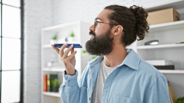 Modern ofiste akıllı telefon kullanan, iş ortamında teknoloji ve iletişim gösteren İspanyol sakallı bir adam..