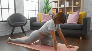 Aktivite kıyafetli bir kadın şık bir oturma odasında yoga yapıyor, sağlık ve sükunet tasvir ediyor..