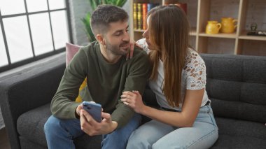 Sevgi dolu bir çift evin içinde bir kanepede rahatlar, rahat bir evde akıllı bir telefonla bir anı paylaşır..