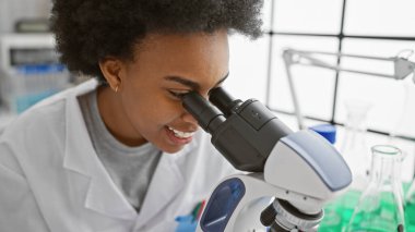Laboratuvar ortamında mikroskop kullanan Afrika kökenli Amerikalı kadın bilim adamı profesyonel bir araştırma ortamını canlandırıyor..