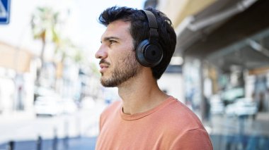 Güneşli bir sokak sahnesinde kulaklık takan yakışıklı İspanyol adam.