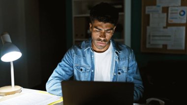 Masa lambası ve dizüstü bilgisayarla geç saatlere kadar çalışan konsantre İspanyol adam.