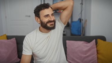 Rahat sakallı bir adam modern bir oturma odasında gülümser, rahatlık, rahatlık ve sıradan bir yaşam tarzı tasvir eder..