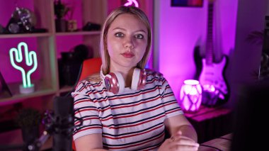 Oyun odasında kulaklık takan sarışın bir kadın. Arka planda neon ışıklar ve gitar var..