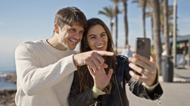 Neşeli bir çift okyanus kenarında neşeli bir selfie çekiyor, ilişkilerini ve güzel kumsal manzarasını vurguluyorlar..