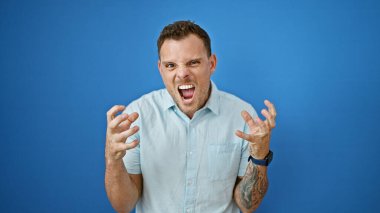 Mavi bir duvarın önünde öfkesini dışa vuran sakallı sinirli genç bir adam..