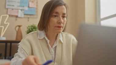 Konforlu bir ofis ortamında dizüstü bilgisayarda çalışan olgun bir kadın.