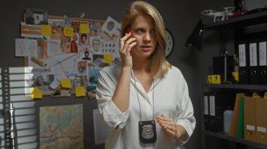 Beyaz gömlekli sarışın bir kadın dedektifin elinde rozet var ve bir ofiste kanıt panosuyla konuşuyor..