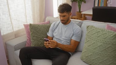 Yeşil yastıklı ve arka plan dekoru olarak kapalı salonda akıllı telefon kullanan yakışıklı bir adam.