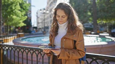 Genç İspanyol kadın Thai Baht 'ı şehir parkında fıskiyeli tutuyor.