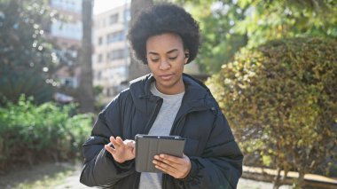 Kablosuz kulaklık ve tablet kullanan kıvırcık saçlı Afrikalı Amerikalı kadın..