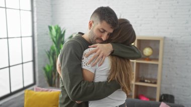 Sevgi dolu bir çift, rahat bir oturma odasında kucaklaşır. Sevgisini ve beraberliğini, rahat bir yuva ortamında ifade eder..