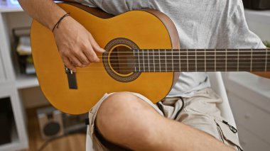 Kapalı mekanda akustik gitar çalan, telleri tıngırdatan, müzikal bir atmosfer yaratan bir adam.